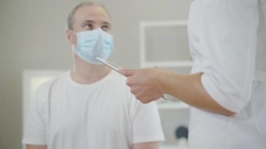 Tanımlanamayan doktor, yüz maskesi takmış orta yaşlı bir adamın tıbbi geçmişini alıyor. Beyaz kadın doktor hastalık ya da hastalık belirtileri soruyor ve verileri tablete kaydediyor. Covid-19 salgını.
