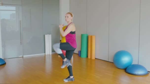 Visão lateral amplo tiro de treinador de fitness levantando perna e falando. Retrato de desportista profissional confiante que treina pessoas no ginásio. Exercício de mulher branca atlética dentro de casa. — Vídeo de Stock