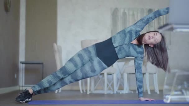 Ampia foto di donna caucasica magra in abbigliamento sportivo che lavora sul tappetino da ginnastica. Ritratto di giovane sportiva bruna che si allena al chiuso. Adatto a signora snella che si esercita a casa o in palestra. — Video Stock