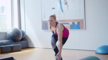 Güçlü bir sporcunun aynadaki yansıması içeride antrenman yapıyor. Spor salonunda spor yapan beyaz bir kadının geniş açılı çekimi. Kendine güvenen sporcu kadının portresi..