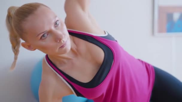 Portrait d'une sportive concentrée faisant de l'exercice en position de planche latérale. Jeune femme caucasienne forte formation à l'intérieur. Femme blonde confiante travaillant dans la salle de gym. — Video