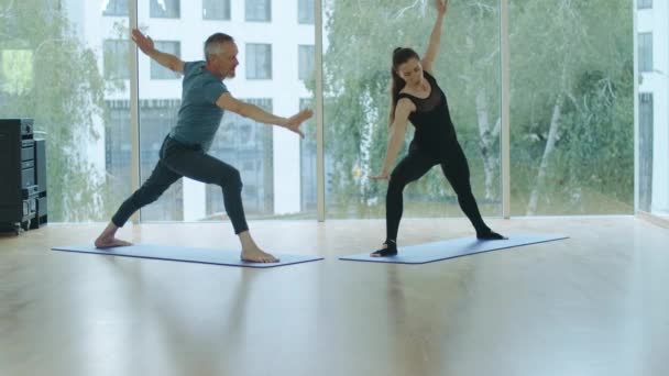 Amplio plano de hombre y mujer practicando yoga en el gimnasio. Retrato de yogui masculino y femenino haciendo ejercicios en la esterilla de ejercicio. Entrenamiento seguro de los deportistas caucásicos en interiores. — Vídeo de stock