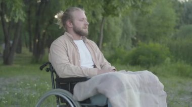 Tekerlekli sandalyede oturan düşünceli genç adamın portresi. Parkta ona koşan ve sarılan neşeli güzel bir kadın gibi. Mutlu engelli erkek arkadaş yaz akşamları sevgilisiyle çıkıyor..