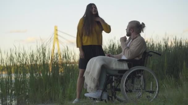 Jeune femme agacée hurlant et laissant l'homme handicapé seul en fauteuil roulant. Conflit de couple caucasien argumenté en soirée d'été sur la rive. Paralysé déprimé gars fermeture visage avec les mains. — Video
