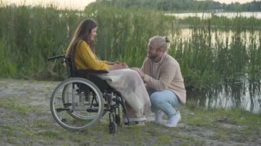 Gün batımında nehir kıyısında engelli bir kadına nişan yüzüğü veren mutlu beyaz adam. Romantik erkek arkadaşın portresi engelli kız arkadaşına evlenme teklif ediyor..