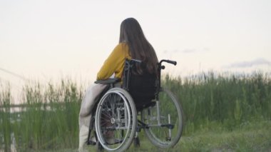 Tekerlekli sandalyedeki yalnız kadının nehir kıyısında oturuşu. Esmer, beyaz, engelli bir kadının yaz akşamını dışarıda yalnız geçirmesi. Yalnızlık ve sakatlık.