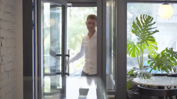 Portrét pohledného mladíka, jak vstupuje do kavárny a nastoluje pořádek. Veselý sebevědomý běloch v bílé košili a džíny s přestávkou v obchodním centru kantýny. — Stock video