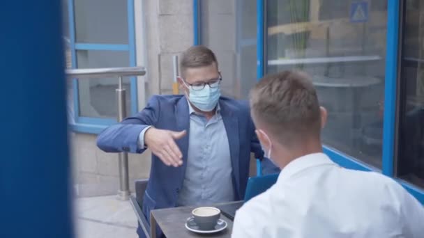 两名戴面具的白人商人在户外咖啡馆握手。有信心的男人在城市举行关于Covid-19大流行病的商务会议。Coronavirus生活方式. — 图库视频影像