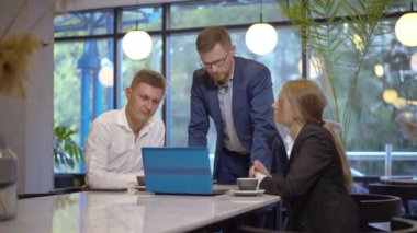 Takım elbiseli ve gözlüklü bir adam iş ortaklarına dizüstü bilgisayarda sunum yapıyor. Kafe 'de yemek yiyen başarılı, kendine güvenen beyaz insanların portresi. Takım çalışması ve işbirliği kavramı.