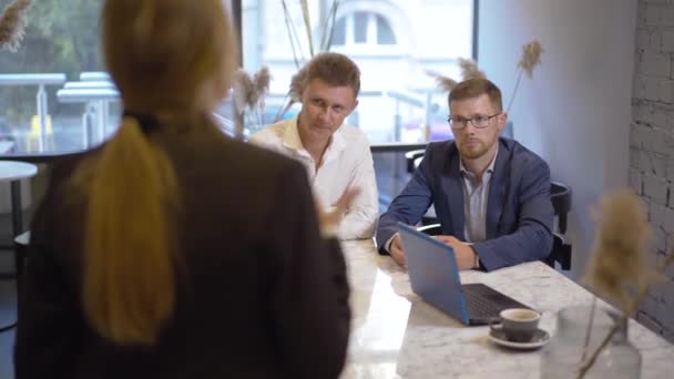 Fokuserade affärsmän sitter vid bordet och lyssnar på ung kvinna prata och gestikulera. Oigenkännlig kaukasisk affärskvinna som förklarar start för partners eller kollegor på kafé. — Stockvideo