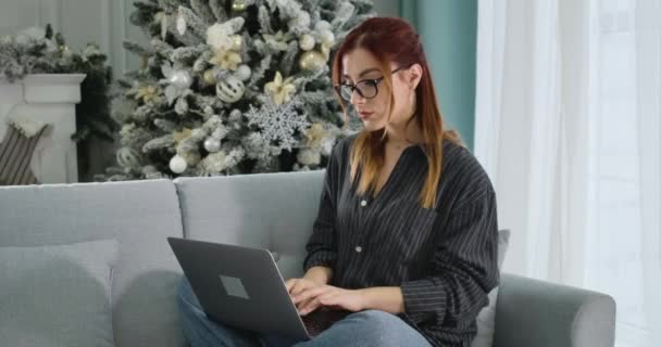 Серьёзно сконцентрированная рыжая женщина, печатающая на клавиатуре ноутбука в Новый год. Портрет уверенного кавказского фрилансера, работающего дистанционно в канун Рождества. Штаб-квартира кинотеатра 4k ProRes. — стоковое видео