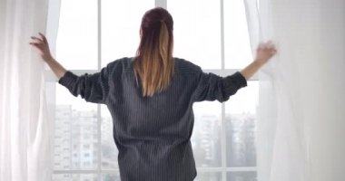 Mutlu, dinlenmiş bir kadının perdeleri açması ve sabahları esnemesi. Tasasız, genç, beyaz bir bayan uyanıyor ve şehre bakıyor. Kamera devreye giriyor. Sinema 4k ProRes Merkezi.