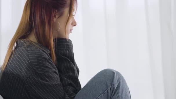 Herzzerreißende junge Frau sitzt vor dem Fenster und denkt nach. Seitenansicht Porträt der traurigen schönen kaukasischen Dame nach der Trennung. Frustration und Depression. — Stockvideo