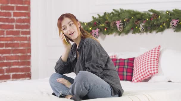 Portret szczęśliwej kobiety słuchającej komplementów i rozmawiającej przez telefon. Zrelaksowana, beztroska biała dama ciesząca się Wigilią w sypialni w domu. Koncepcja nowego roku wakacyjnego. — Wideo stockowe