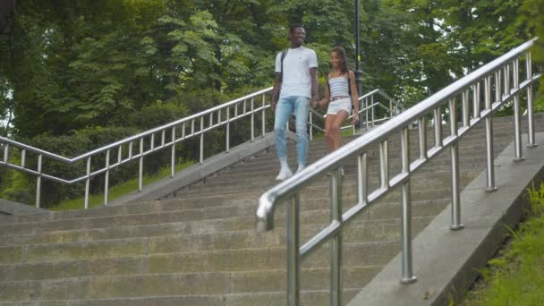 Gelukkige Afro-Amerikaanse broer en zus lopen de trap af in het park en vertrekken. Portret van een mooi klein meisje en een knappe jongeman die buiten wandelen op zonnige zomerdag. — Stockvideo