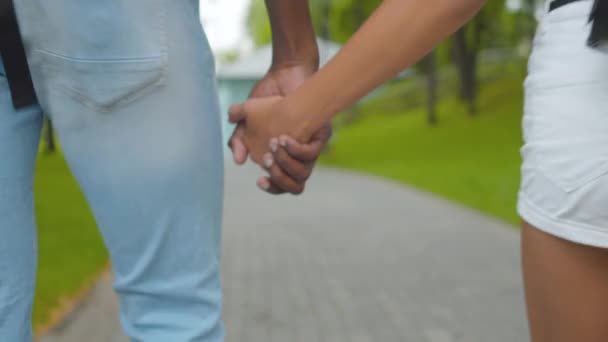 Primer plano de las manos afroamericanas masculinas y femeninas abrazándose entre sí con el hombre y la niña que se alejan a lo largo del callejón del parque. Relajados hermano y hermana paseando al aire libre en el soleado día de verano. — Vídeos de Stock