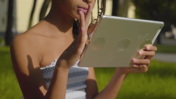Unerkennbares afroamerikanisches Mädchen, das im Sommerpark soziale Medien auf dem Tablet nutzt. Kinder surfen im Internet und sitzen im Sonnenlicht im Freien. Konzept der Geräteabhängigkeit der Generation Z. — Stockvideo