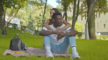 Mutlu Afrikalı Amerikalı kız kardeş güneşli yaz parkında kardeşine sarılıyor. Kameraya bakıp gülümseyen neşeli kardeşlerin portresi. Neşeli genç adam ve küçük kız dışarıda dinleniyor..