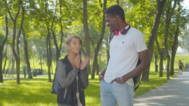 Neşeli genç bir adam ve küçük bir kızın güneşli parkta dikilip konuşmalarının portresi. Mutlu Afrika kökenli Amerikalı kardeşler hafta sonlarının tadını çıkarıyorlar..