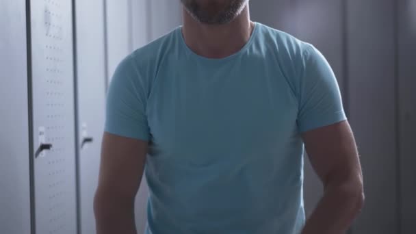 Unerkennbarer Sportler, der sein blaues T-Shirt auszieht und die Kamera mit Kleidung bedeckt. Athletischer Kaukasier wechselt nach Training in Turnhalle-Umkleide. — Stockvideo