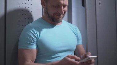 Spor salonunda akıllı telefon kullanan gülümseyen sakallı bir sporcu. İnternette sörf yapan ya da spor yaptıktan sonra sosyal medyayı kullanan mutlu beyaz adamın portresi. Yaşam tarzı kavramı.