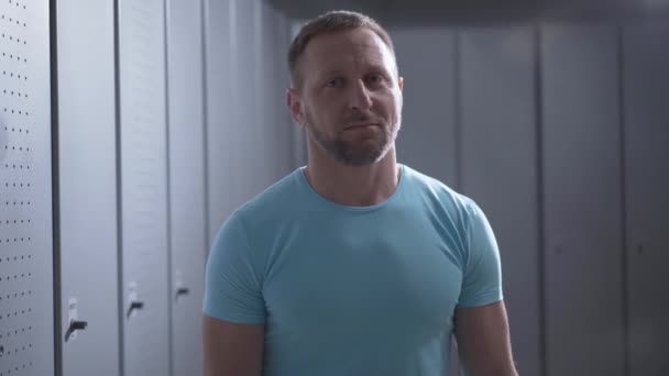 Portrait of confident sportsman crossing hands and smiling at camera. Adult bearded Caucasian man posing in gym locker room. Positive guy standing in dressing room. Sport concept. — Stock Video