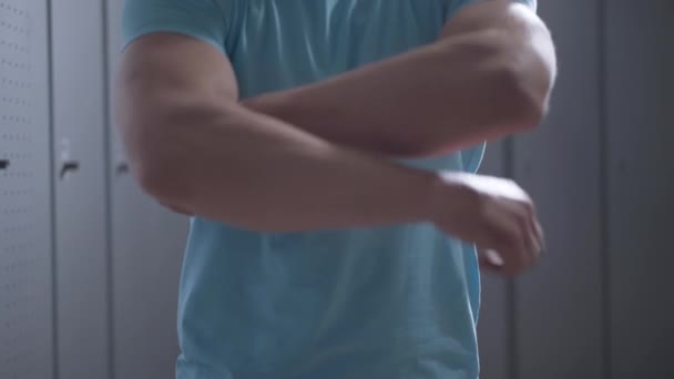 Felismerhetetlen, erős, kék pólós sportoló keresztbe tett kézzel áll az öltözőben. Sportos kaukázusi férfi pózol tornaterem öltözőjében edzés előtt vagy edzés után. — Stock videók