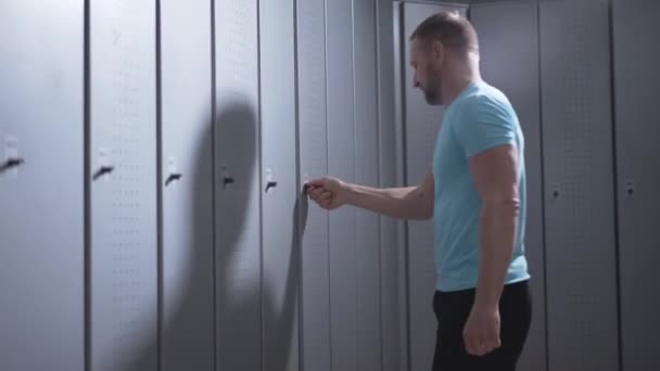 Serious Caucasian man opening locker in gym and using smartphone. Portrait of confident strong sportsman checking e-mails after training. Handsome guy messaging online after workout. — Stock Video