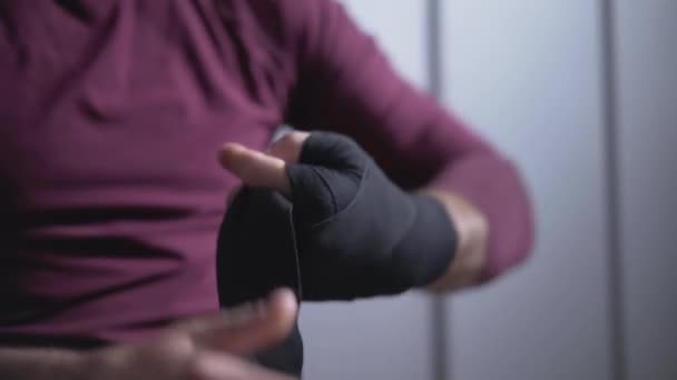 Close-up hand van sterke blanke sportman die zwart verband om de pols wikkelt in de kleedkamer. Onherkenbare bokser bereidt zich voor op training of sparren in de sportschool. Mannelijkheid en vechtsport concept. — Stockvideo