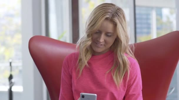 Atractivo rubio mujer caucásica mensajería en las redes sociales en el teléfono inteligente y sonriendo. Retrato de hermosa dama delgada joven navegando por Internet o charlando en línea. Concepto moderno de estilo. — Vídeos de Stock