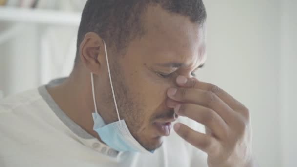 Portret młodego Afroamerykanina kichającego. Chorego faceta w masce, który ma objawy infekcji wirusowej Covid-19. Mężczyzna w szpitalu z powodu pandemii koronawirusowej. — Wideo stockowe