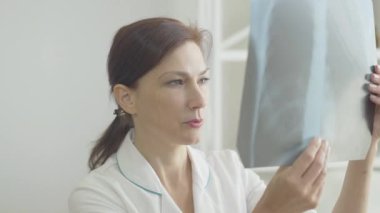Ciddi bir kadın doktor akciğer röntgenine bakıyor. Covid-19 virüsü taşıyan kişinin radyografisini inceleyen beyaz kadın portresi. Koronavirüs hastalarını tedavi eden kendine güvenen bir doktor.