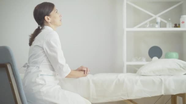 Side view of exhausted Caucasian woman sitting in hospital ward leaning head on hand. Portrait of tired female doctor at workplace. Desperate physician on Covid-19 pandemic. — Stock Video