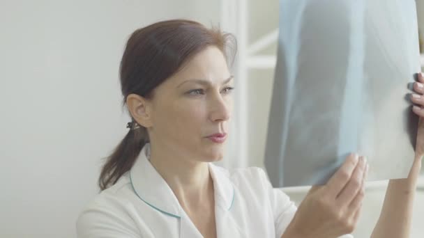 Doctora seria mirando radiografías de pulmones. Retrato de una mujer caucásica profesional que examina la radiografía de una persona con infección viral por Covid-19. Médico de confianza tratando pacientes con coronavirus — Vídeo de stock