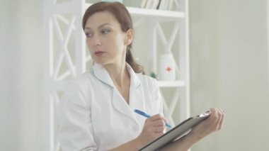 Tıbbi geçmişi dolduran, doktor üniformalı, konsantre beyaz kadın. Hastane için çalışan ciddi profesyonel doktorların portresi. Tıp ve sağlık hizmetleri kavramı.