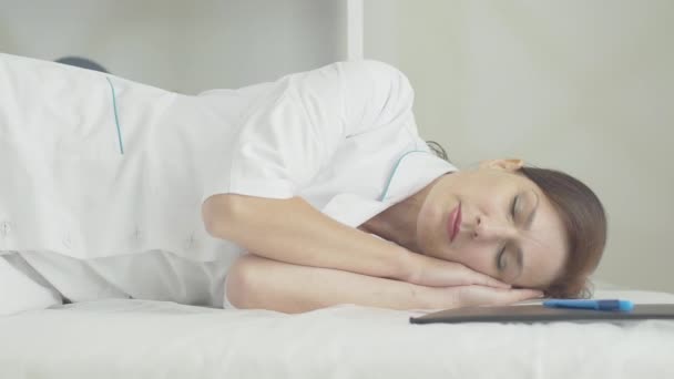 Retrato del doctor exhausto durmiendo en la cama en la sala del hospital. Mujer caucásica medio adulta agotada cansada del brote de Covid-19. Empleado médico que tiene un breve descanso durante el coronavirus. — Vídeos de Stock