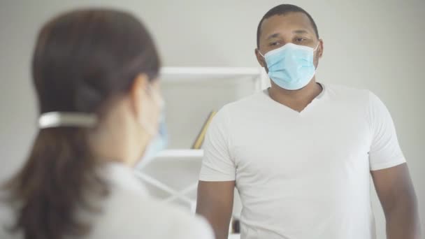 Serious African American man in face mask listening to Caucasian woman and shaking head gesturing yes. Patient agreeing with professional physician. Doctor visit on Covid-19 pandemic. — Stock Video