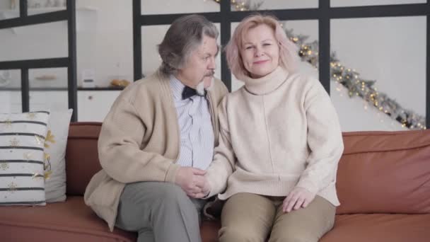 Heureux couple caucasien âgé assis sur le canapé la veille de Noël et bavarder. Portrait de charmant vieil homme et femme reposant sur le Nouvel An à la maison ensemble. Amour éternel, temps des fêtes. — Video