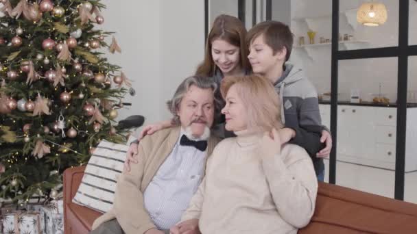 Alegres abuelos y nietos disfrutando de la Navidad con el árbol de Año Nuevo al fondo. Retrato de feliz reunión familiar multigeneracional caucásica en casa en vacaciones. — Vídeos de Stock