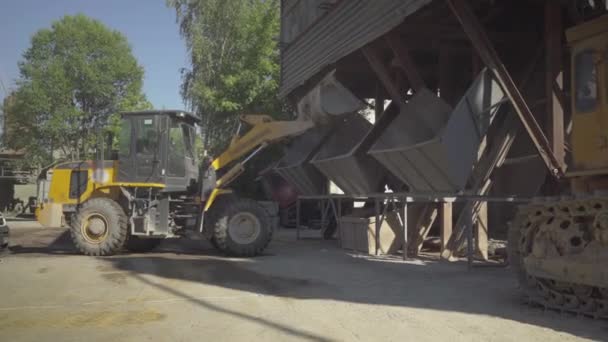 Amplio plano de tractor descargando material a granel en el sitio de producción en el día soleado. Maquinaria que trabaja en la fábrica de cemento al aire libre. Industria del hormigón. — Vídeo de stock