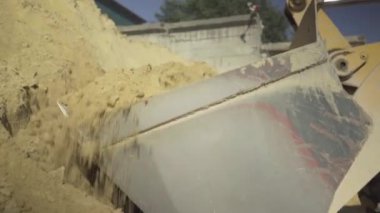 Traktör yükleyicisi sarı kum topluyor ve geriye doğru gidiyor. Fabrika alanında çimento üretimi için malzeme yükleyen endüstriyel makineler. Somut endüstri.