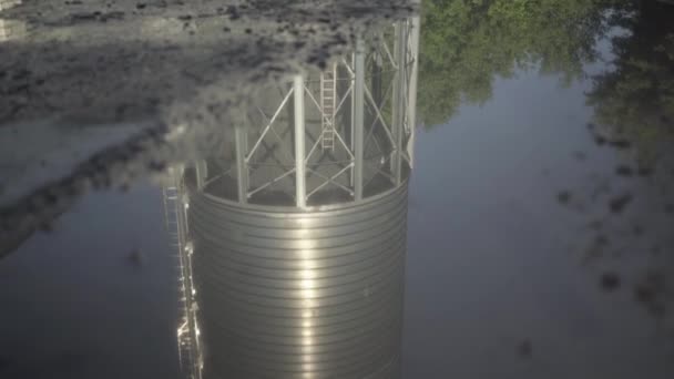 Cámara se mueve hacia abajo a lo largo de la reflexión de gran depósito en paleta clara. Gran silo de almacenamiento de cemento que se refleja en el agua al aire libre en el día soleado. Torre en fábrica de fabricación de hormigón. — Vídeos de Stock