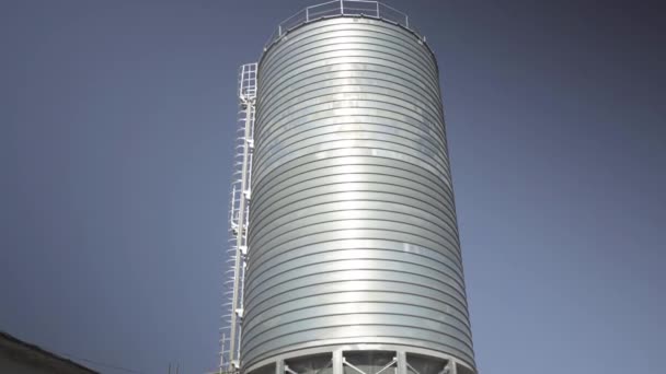 Câmera desce ao longo enorme silo de armazenamento de cimento de aço inoxidável com céu azul claro no fundo. Amplo tiro de grande reservatório na fábrica de concreto. — Vídeo de Stock
