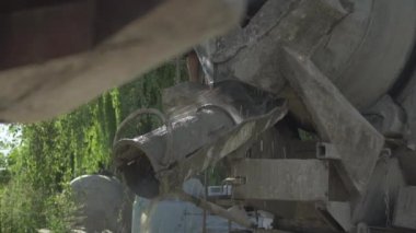 Tanınmayan işçi çimento karıştırıcıyı temizliyor ve beton fabrikasını kurutuyor. Erkek Kafkas çalışanı güneşli bir günde ağır endüstriyel ekipmanların üzerine temiz su döküyor..