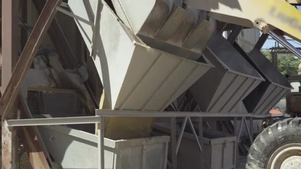 Unloading of sand for cement manufacture on factory outdoors. Industrial tractor pouring bulk material out of bucket into device raising it to cement storage silo. — Stock Video
