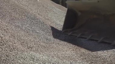 Traktör kovası fabrikaya taş indirirken yan görünüm. Güneşli bir günde üretim alanında malzeme toplama işlemi.