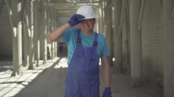 Портрет положительного мастера, смотрящего в камеру и улыбающегося. Взрослый кавказский строитель позирует на стройке. Уверенный человек, стоящий на рабочем месте под солнцем. — стоковое видео
