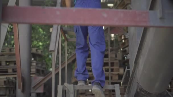 Белый мужчина в форме поднимается по лестнице и поворачивает колесо на конвейере. Профессиональный работник завода регулирует промышленное оборудование на открытом воздухе в солнечный день. — стоковое видео