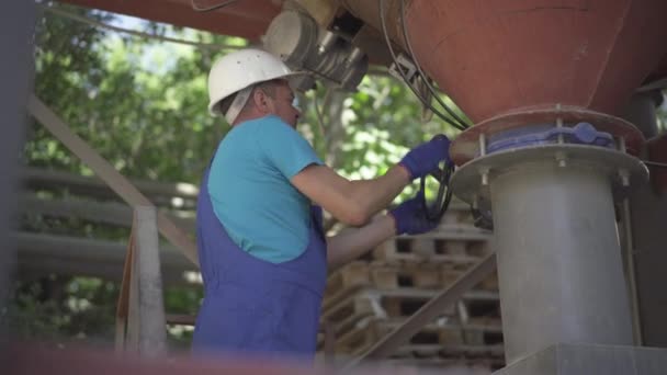 Trabalhador de fábrica sério ajustando equipamentos industriais em planta de fabricação de concreto. Especialista masculino caucasiano confiante ajustando transportador de parafuso de cimento e descendo a escada ao ar livre. — Vídeo de Stock