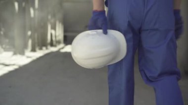 Güneş ışığında şantiyeye giren beyaz kasklı beyaz bir adamın ellerinde. Mavi üniformalı bir erkek müteahhit ve inşaat alanında çalışan eldivenler..